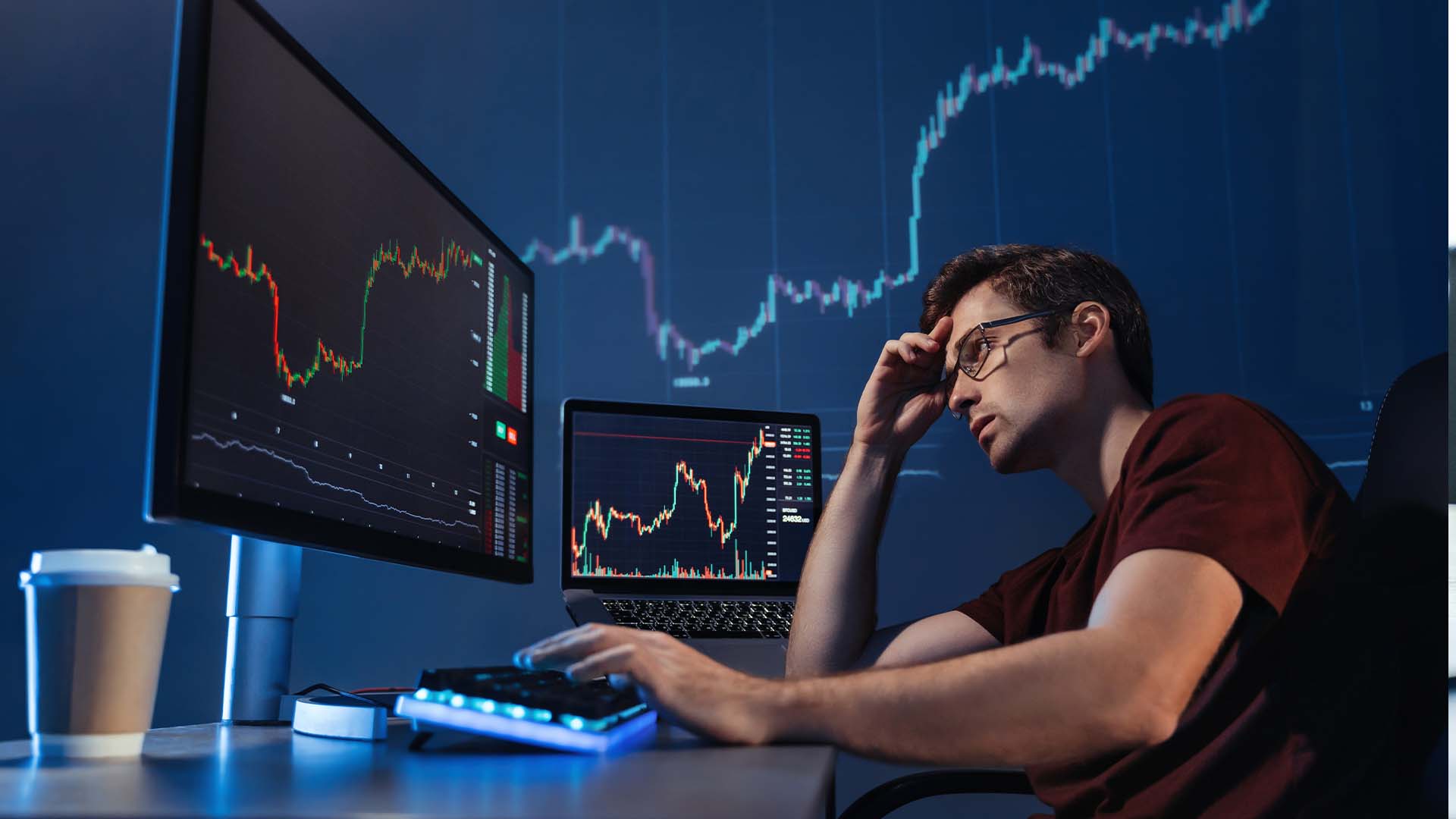 Stressed day trader holding his head while analyzing volatile financial charts on multiple computer screens.