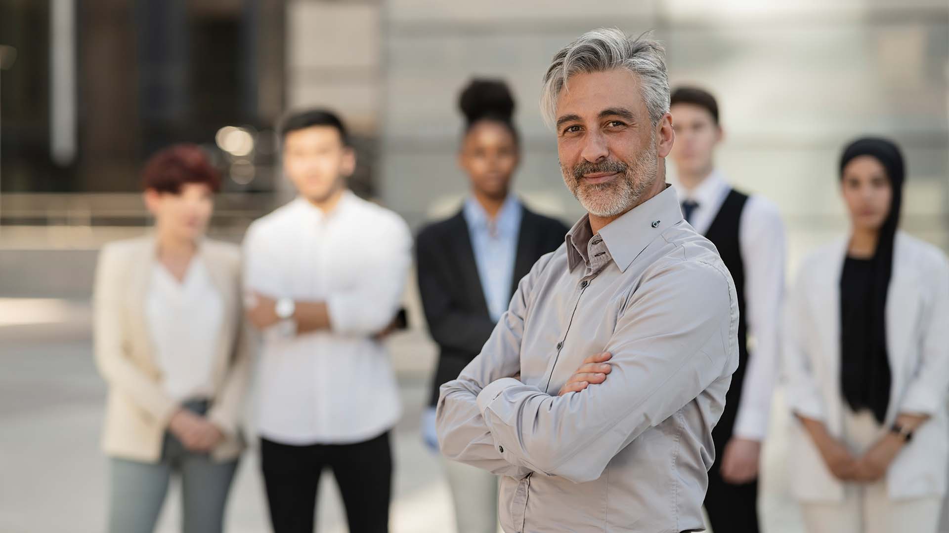 Confident male institutional sales leader standing in front of his diverse corporate team.
