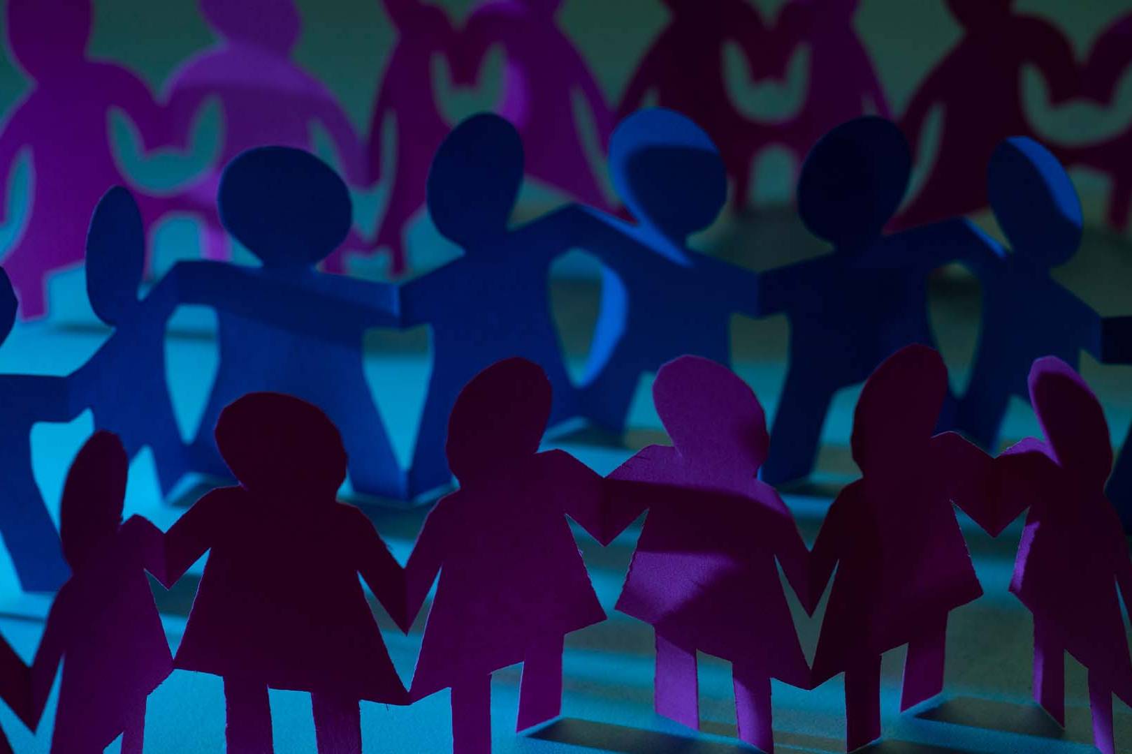 Rows of interconnected paper cutout figures holding hands in a circle under moody blue and purple lighting.