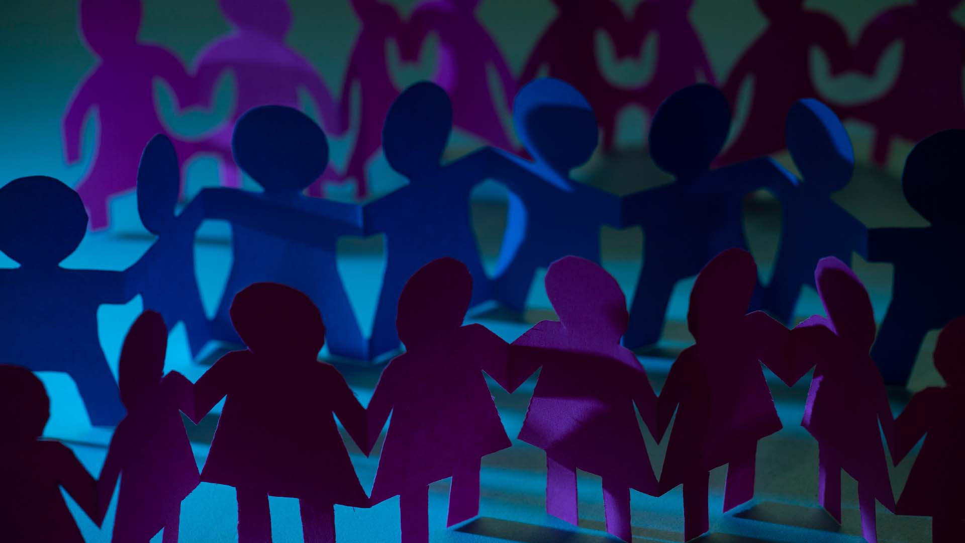 Rows of interconnected paper cutout figures holding hands in a circle under moody blue and purple lighting.
