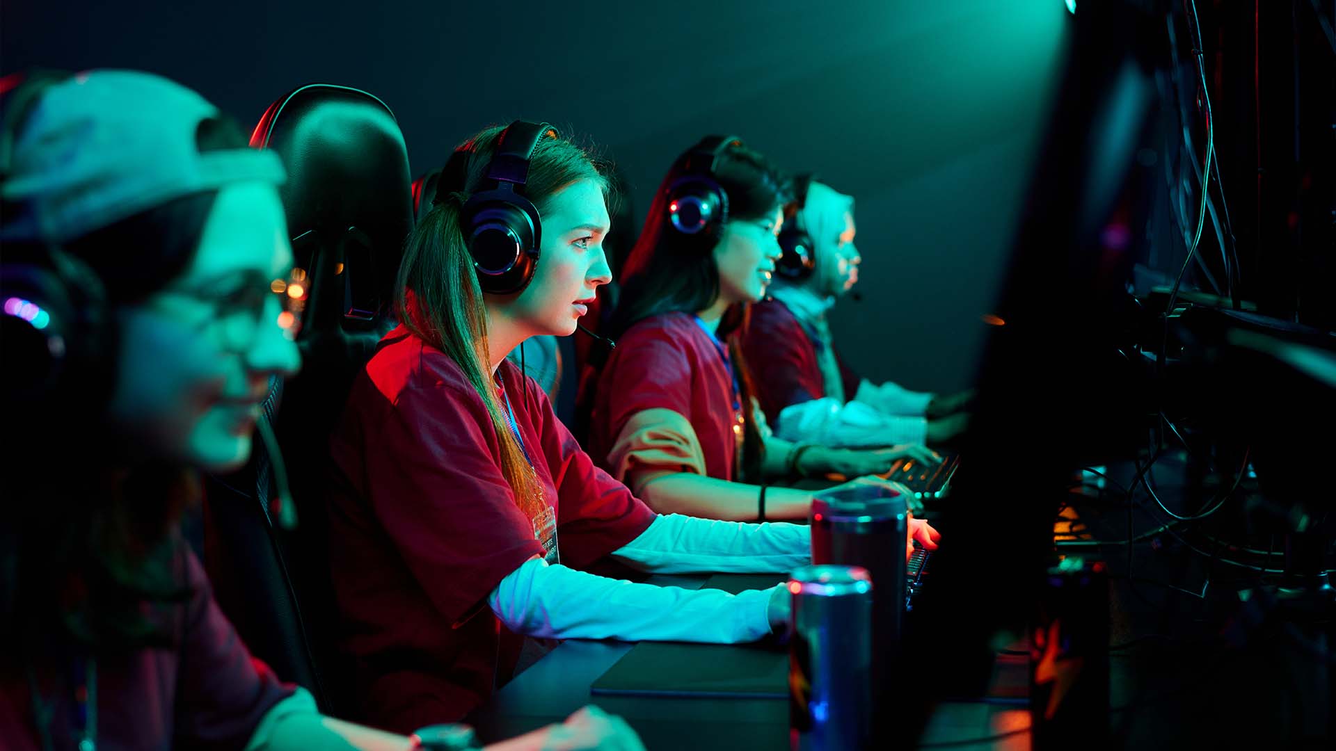 A team of female professional gamers wearing headsets competing at a dimly lit esports tournament.