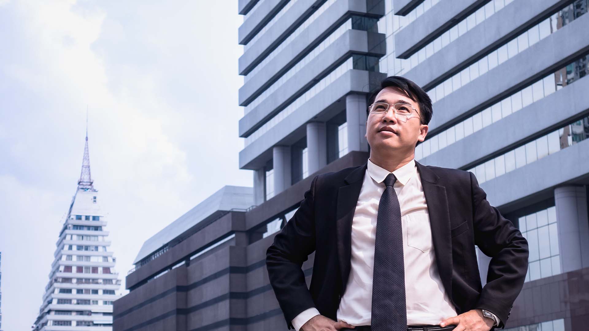 Confident male real estate developer standing in front of modern commercial city skyscrapers.