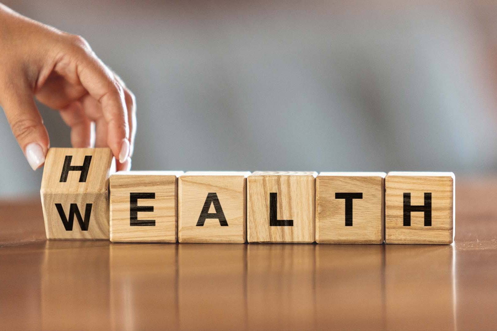 A hand turning a wooden block to change the word WEALTH to HEALTH, representing wealth guilt therapy.