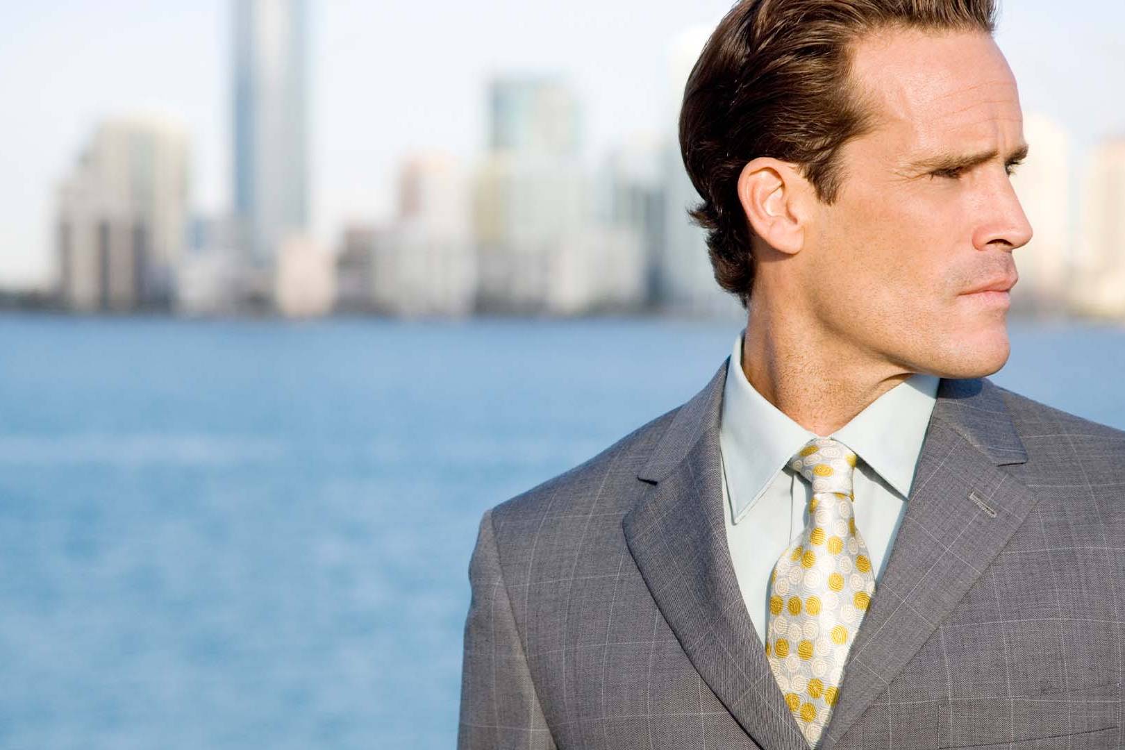 Serious professional man in a grey suit looking away against a city skyline, representing white collar defense law burnout.