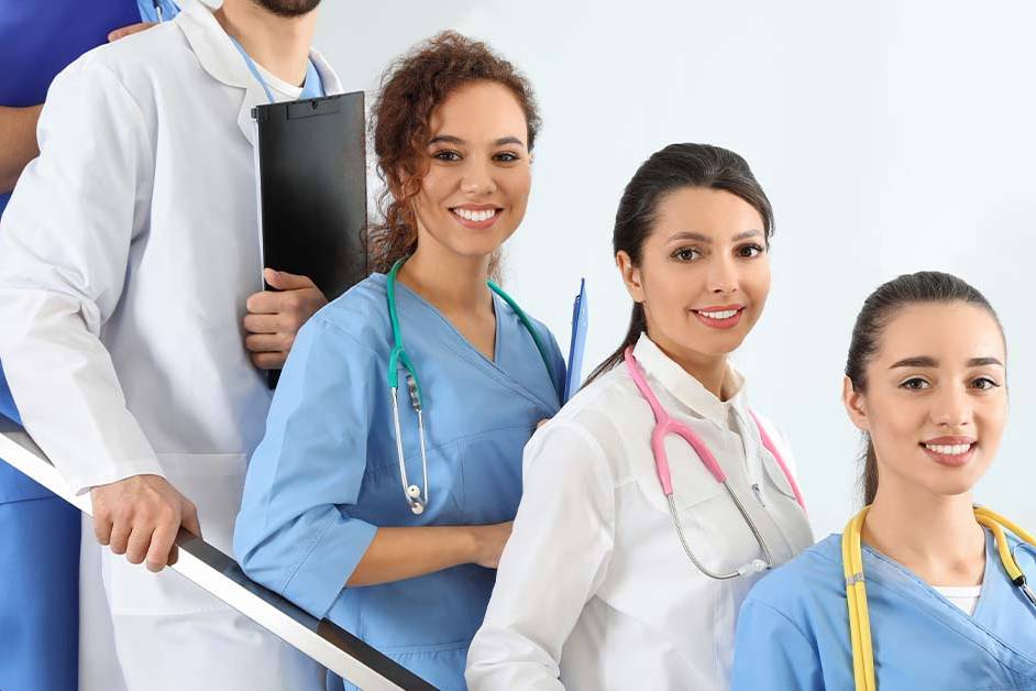 A group of smiling young physicians and medical students in white coats and blue scrubs with colorful stethoscopes stand together on a staircase, representing a medical society's members.