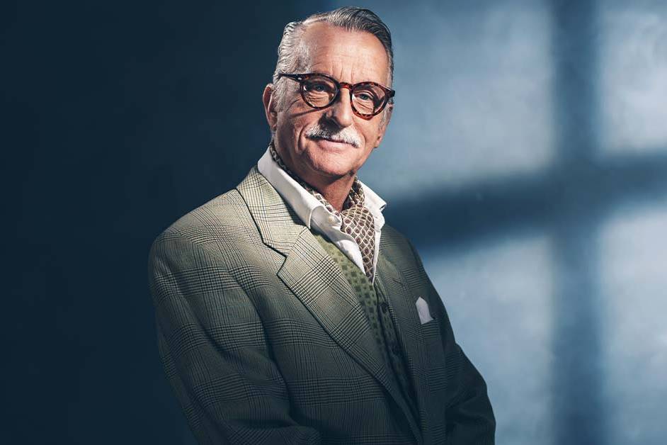 A distinguished older gentleman in a tailored plaid suit and cravat smiling confidently, featured image for the article Therapy for Acquired Founders Inside the Acquirer.