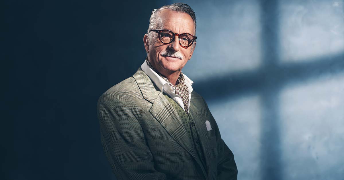 A distinguished older gentleman in a tailored plaid suit and cravat smiling confidently, featured image for the article Therapy for Acquired Founders Inside the Acquirer.