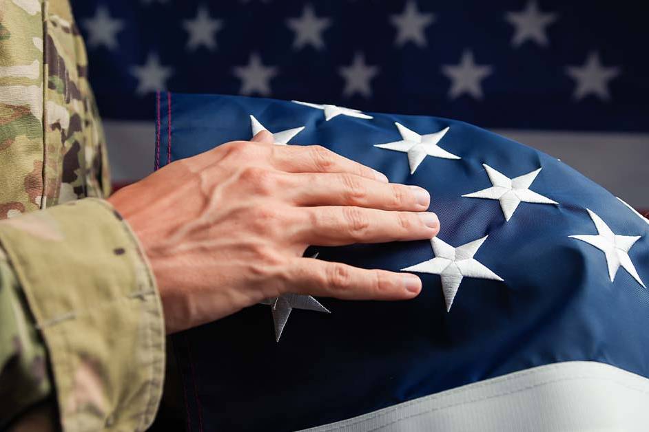 A close-up of a service member in camouflage uniform resting their hand on a folded American flag, featured image for the article Therapy for Active-Duty Flag and General Officers.
