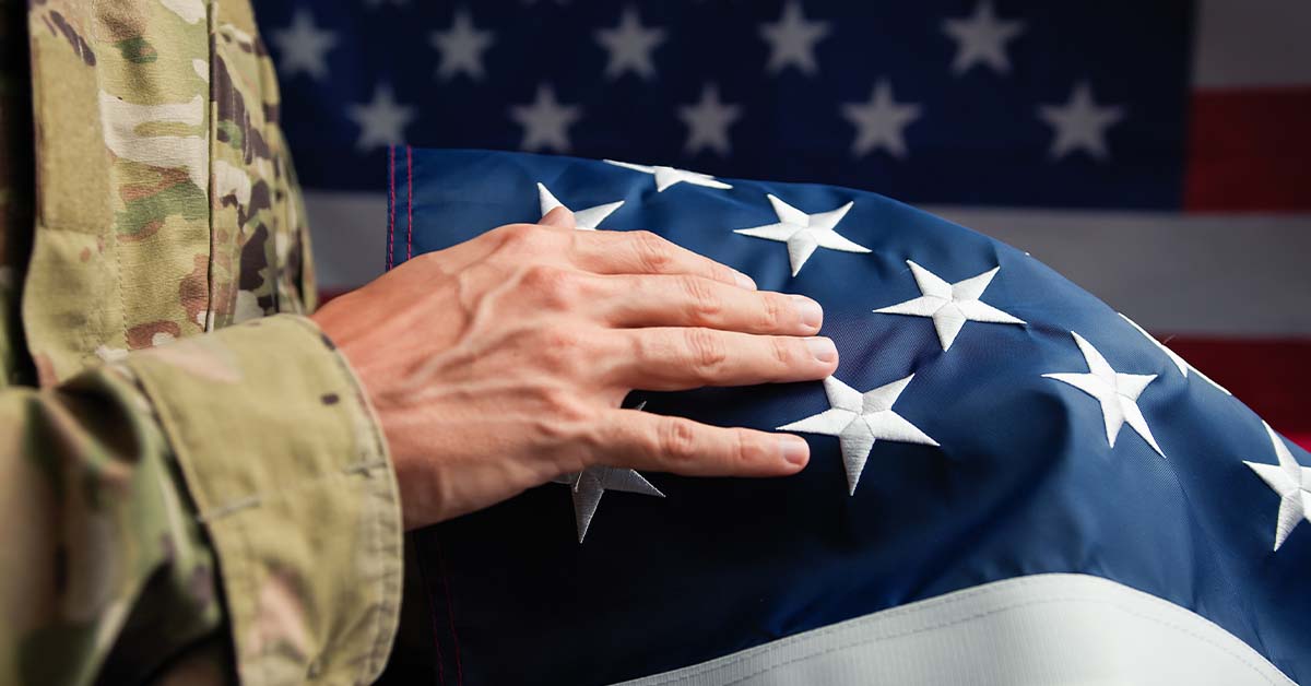 A close-up of a service member in camouflage uniform resting their hand on a folded American flag, featured image for the article Therapy for Active-Duty Flag and General Officers.