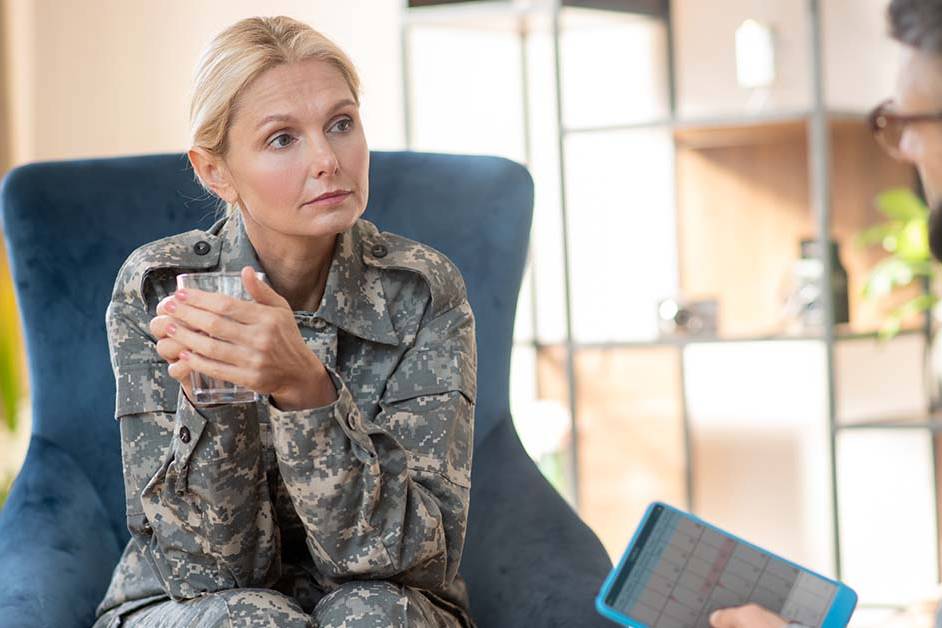 A woman in a military camouflage uniform sitting in a comfortable blue chair speaking with a therapist, featured image for the article Therapy for Active-Duty Military Officer Spouses.