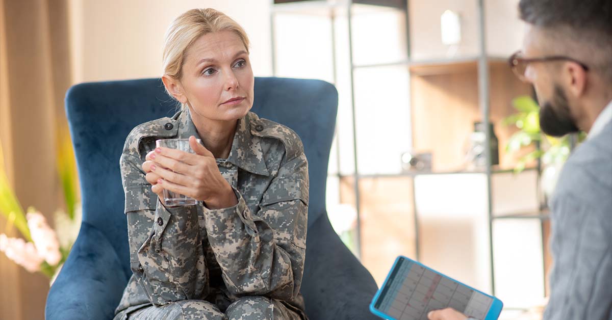 A woman in a military camouflage uniform sitting in a comfortable blue chair speaking with a therapist, featured image for the article Therapy for Active-Duty Military Officer Spouses.