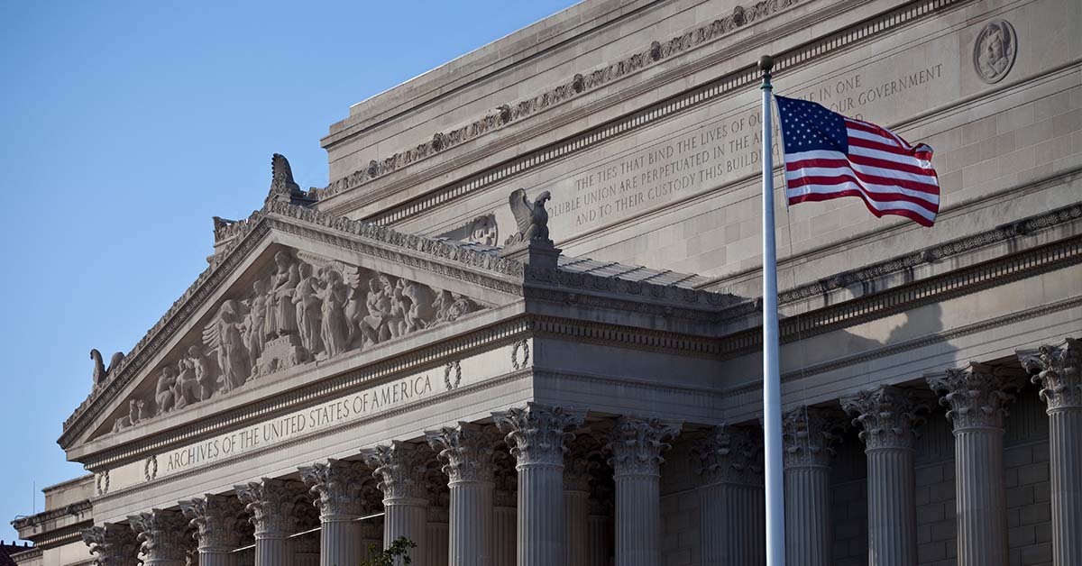 The neoclassical facade of the National Archives building with an American flag flying in the foreground, featured image for the article Therapy for Attorneys With State Bar Reporting Concerns.