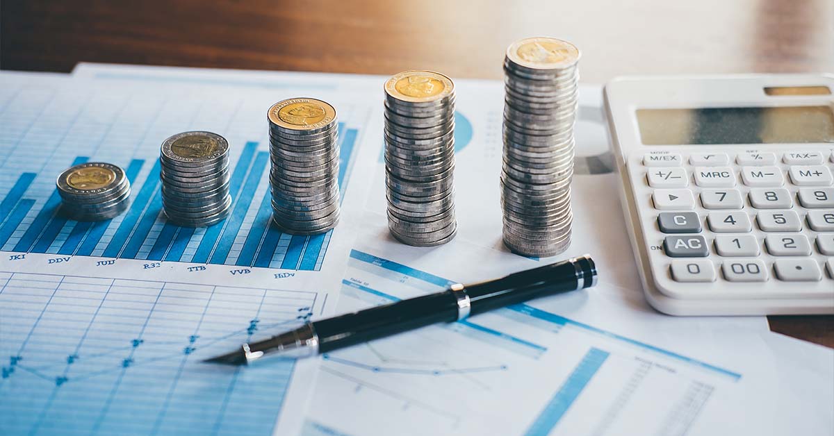 Ascending stacks of coins, a black pen, and a calculator resting on printed financial charts, featured image for the article Therapy for Big Four Accounting Partners.