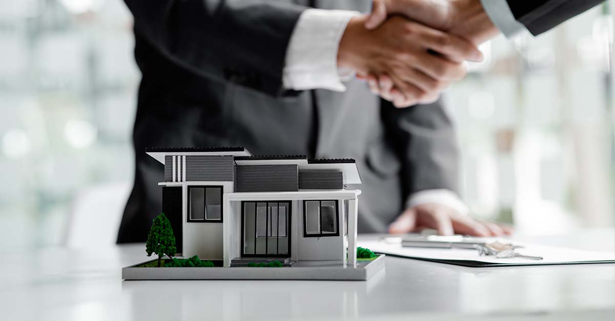 A scale model of a modern house with two professionals in suits shaking hands in the blurred background, featured image for the article Therapy for Big Law Real Estate Partners.