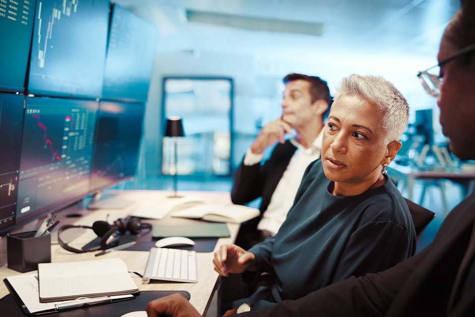 A focused team of financial professionals analyzing complex market data on a multi-monitor display, featured image for the article Therapy for Buy-Side Equity Research Analysts.