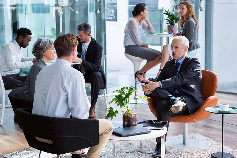 A senior executive in a dark suit speaking with a colleague in a bright corporate lounge, featured image for the article Therapy for Charlotte Banking Executives. Option 2 (Keyword Focused): Corporate financial professionals meeting in a modern office lobby representing mental health therapy for Charlotte banking executives.