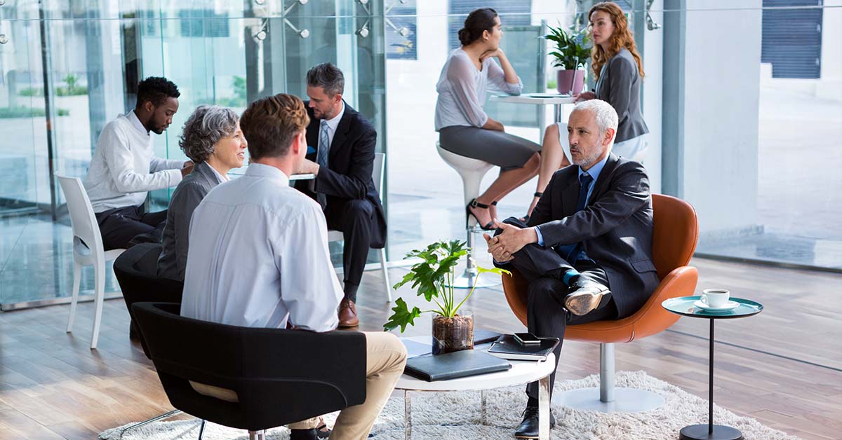 A senior executive in a dark suit speaking with a colleague in a bright corporate lounge, featured image for the article Therapy for Charlotte Banking Executives. Option 2 (Keyword Focused): Corporate financial professionals meeting in a modern office lobby representing mental health therapy for Charlotte banking executives.