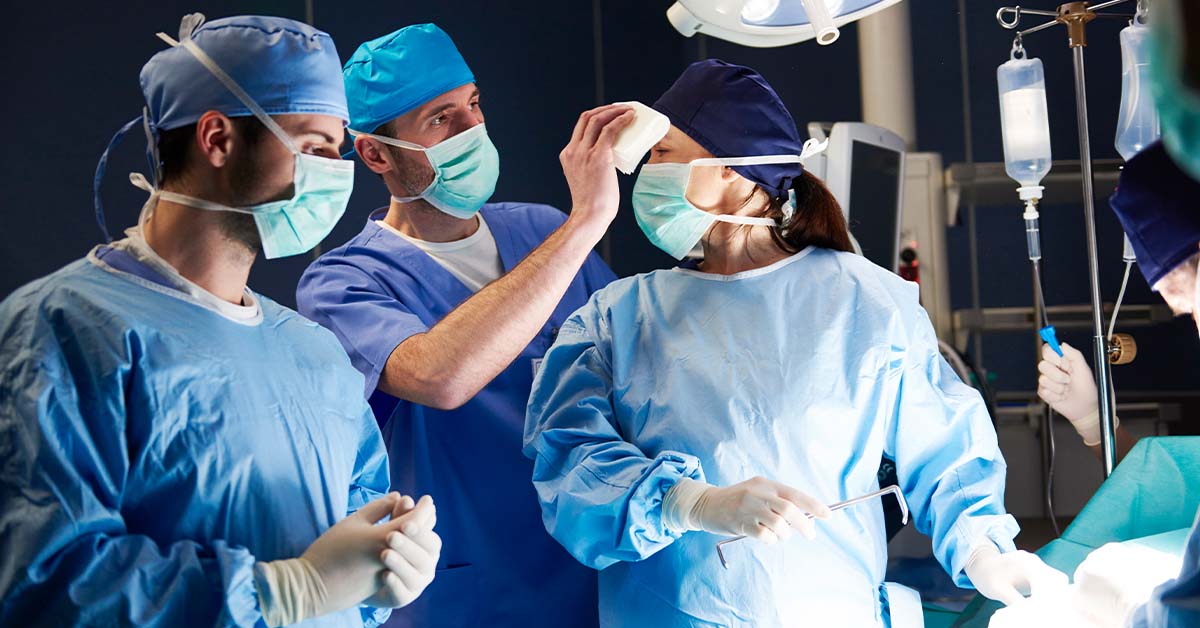 An assistant wiping the brow of a female surgeon in the middle of a tense operation, featured image for the article Therapy for Chicago Surgeons.
