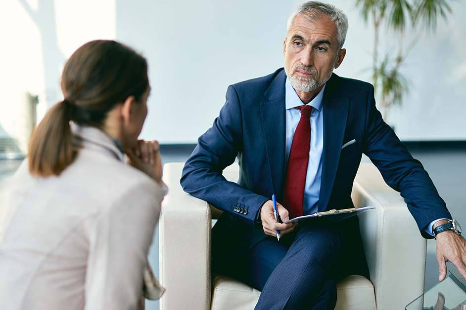 A distinguished male executive in a blue suit and red tie listening intently to a colleague during a meeting, featured image for the article Therapy for Chief Risk Officers.