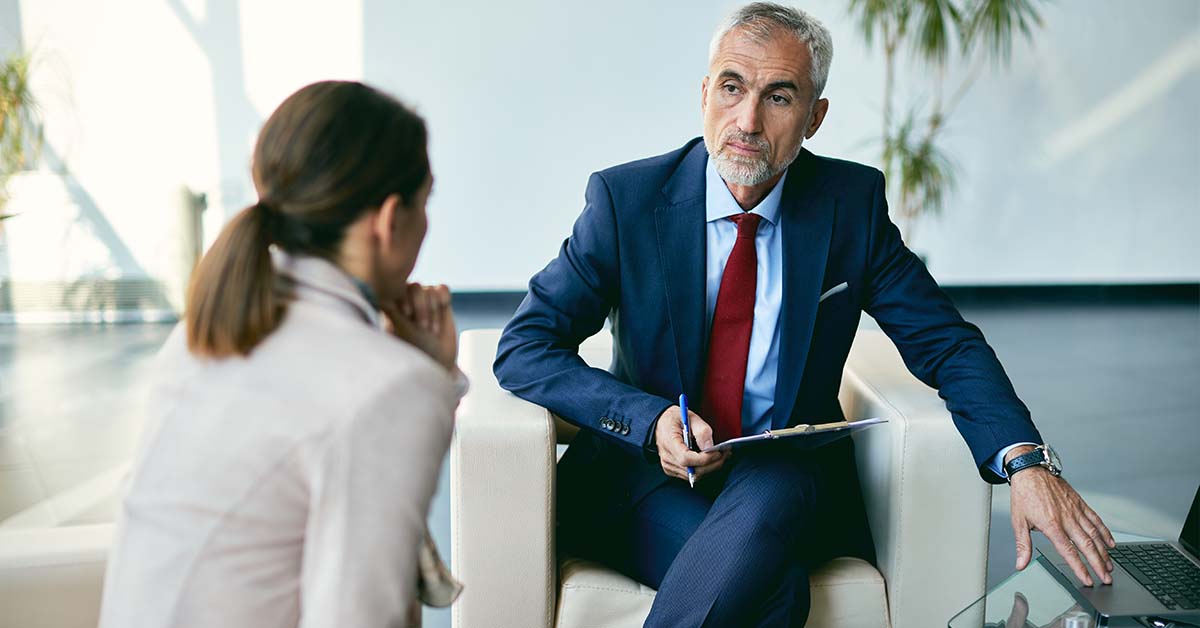 A distinguished male executive in a blue suit and red tie listening intently to a colleague during a meeting, featured image for the article Therapy for Chief Risk Officers.