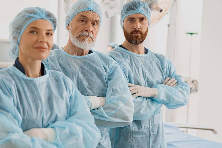 Three medical professionals in blue surgical gowns and caps standing with arms crossed in a clinical setting, featured image for the article Therapy for Chronic Insomnia in Surgeons and ICU Physicians.