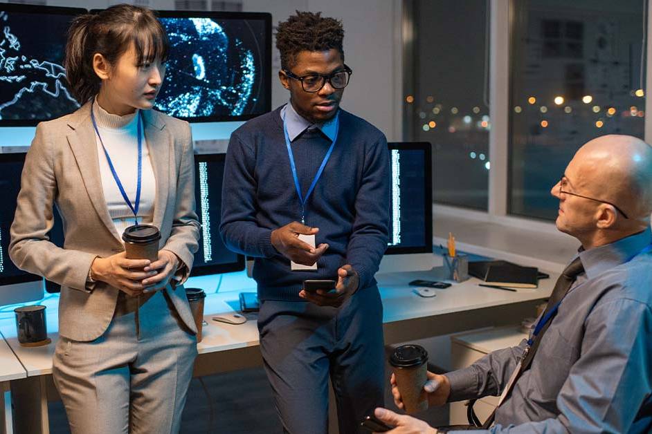Three diverse cybersecurity professionals wearing security lanyards collaborating in a dark, high-tech control room, featured image for the article Therapy for Cleared Cybersecurity Professionals.