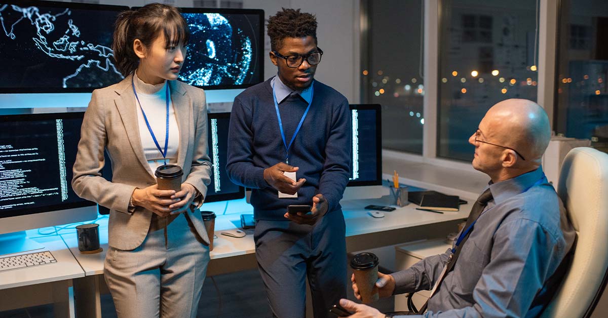 Three diverse cybersecurity professionals wearing security lanyards collaborating in a dark, high-tech control room, featured image for the article Therapy for Cleared Cybersecurity Professionals.