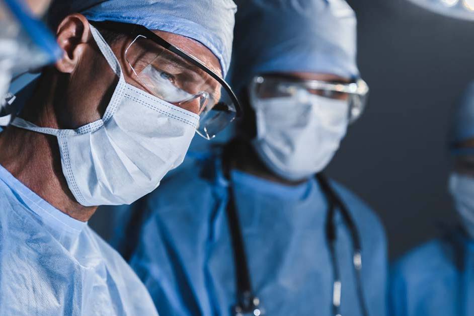 A close-up of a highly focused surgical team in blue scrubs, masks, and safety glasses performing an operation, featured image for the article Therapy for Community General Surgeons.