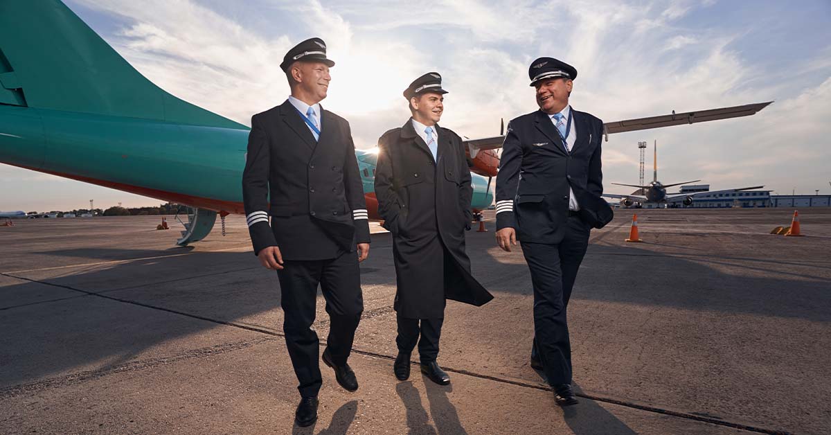 Three pilots in uniform walking together on an airport tarmac at sunset, featured image for the article Therapy for Corporate Jet Pilots. Option 2 (Keyword Focused): Professional aviation crew walking near an aircraft representing mental health therapy and burnout support for corporate jet pilots.