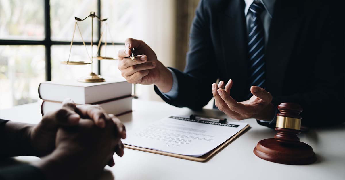 Two professionals discussing a contract agreement at a desk with a gavel and scales of justice, featured image for the article Therapy for DC Big Law Attorneys.