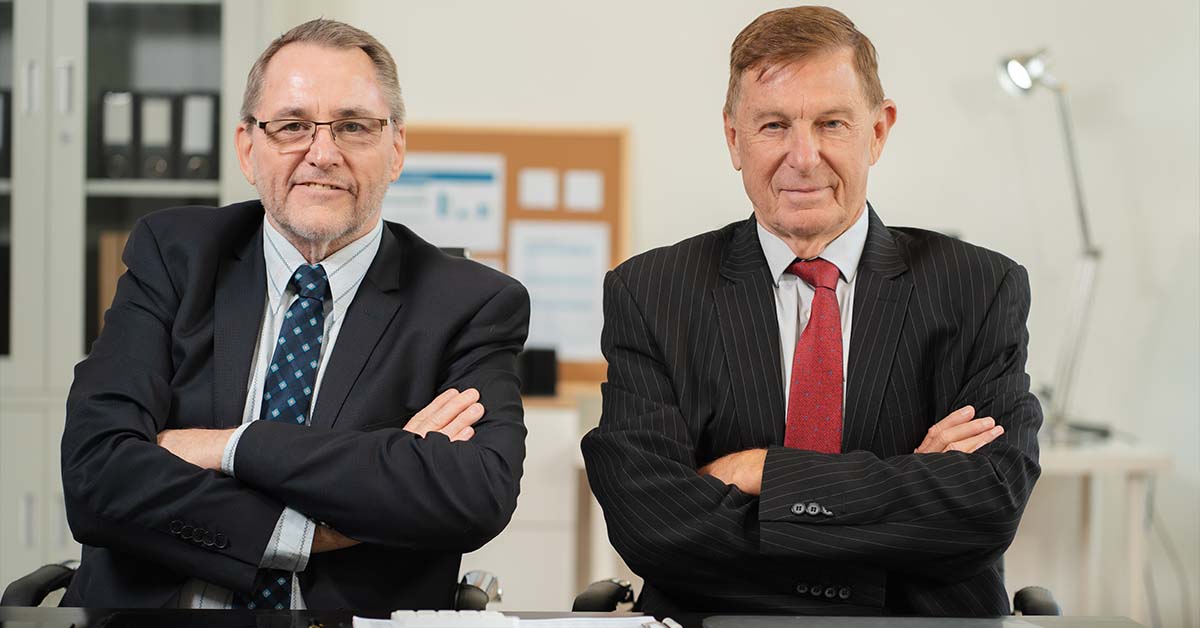 Two senior male financial executives in suits sitting with arms crossed in an office setting, featured image for the article Therapy for Dallas Hedge Fund and Asset Manager Principals.