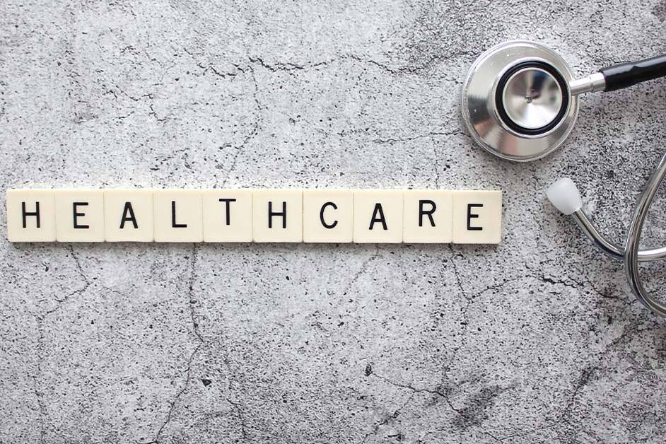 Wooden letter tiles spelling HEALTHCARE next to a silver stethoscope on a grey concrete surface, featured image for the article Therapy for Healthcare Services PE Investors.