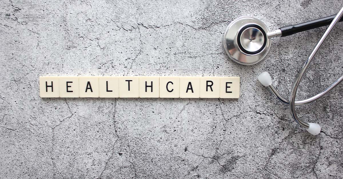 Wooden letter tiles spelling HEALTHCARE next to a silver stethoscope on a grey concrete surface, featured image for the article Therapy for Healthcare Services PE Investors.