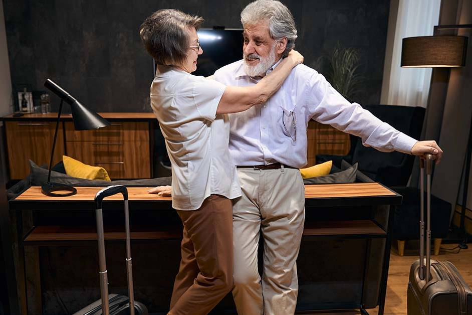 An older couple embracing warmly next to their rolling luggage in a modern living space, featured image for the article Therapy for High-Achievers Returning From Leave.