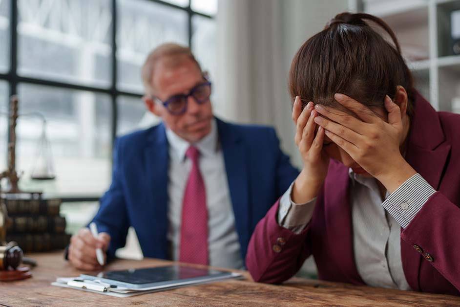 A distressed female lawyer covering her face with her hands at a desk next to a gavel and scales of justice, featured image for the article Therapy for High-Functioning Depression in Lawyers.