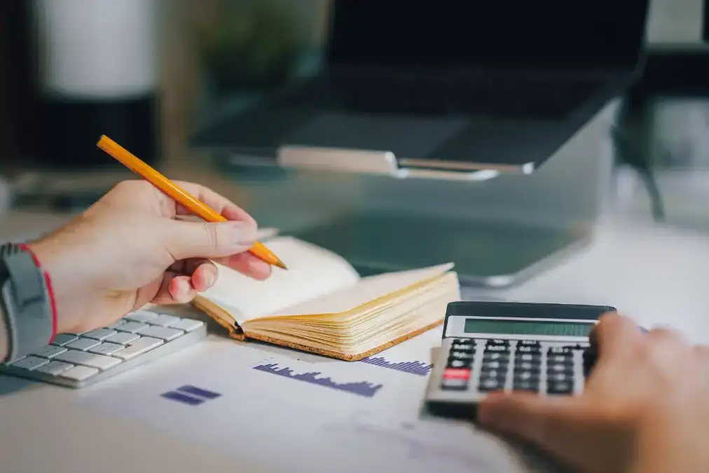 A calm desk with a notebook, calculator, and coffee, planning a monthly budget by a window.