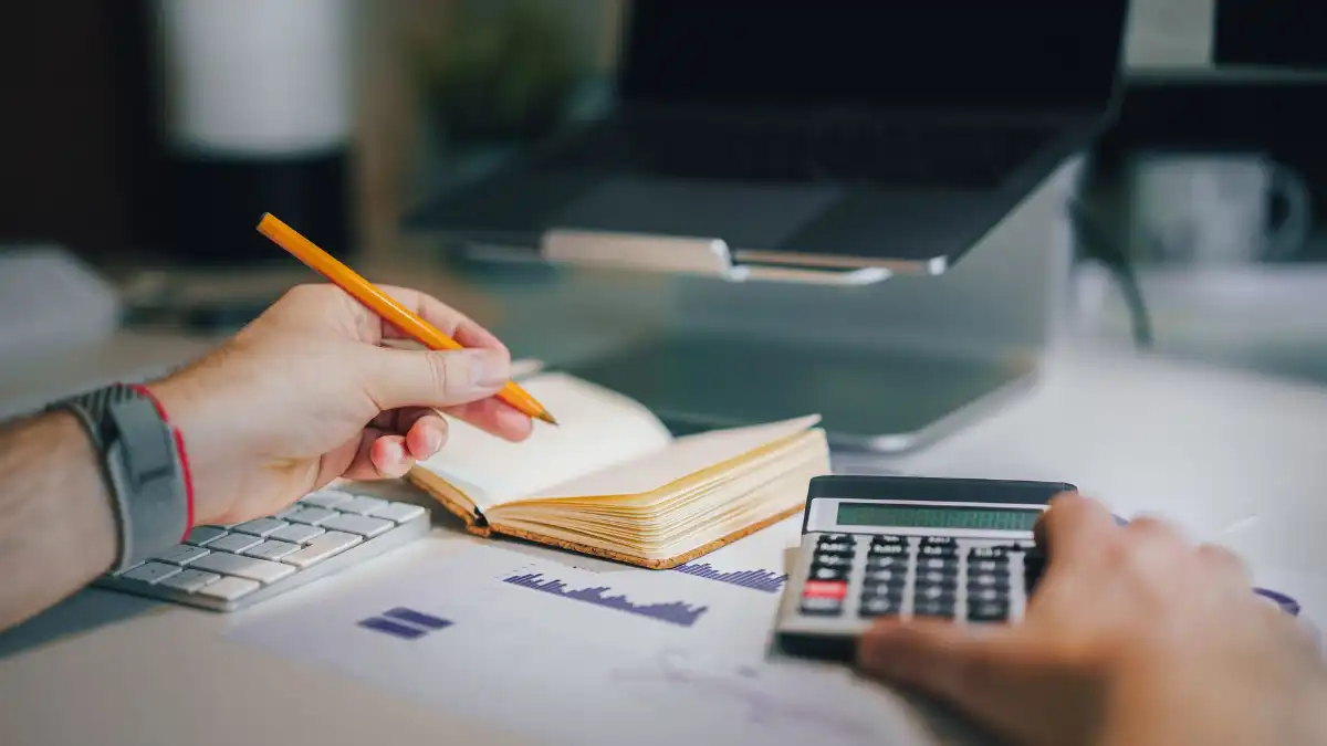 A calm desk with a notebook, calculator, and coffee, planning a monthly budget by a window.