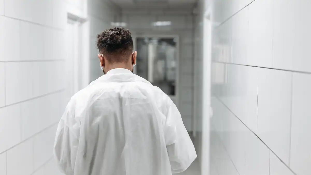 A tired physician standing alone in a quiet hospital corridor at the end of a long shift.