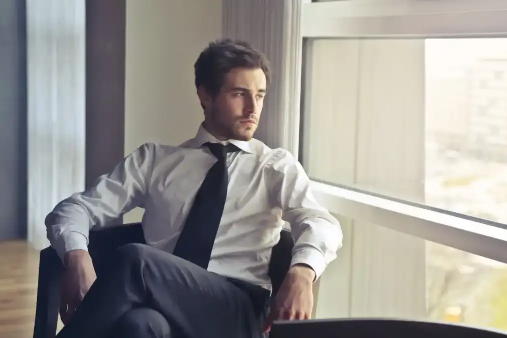 An executive sitting thoughtfully in a calm modern office, gazing out a floor-to-ceiling window.