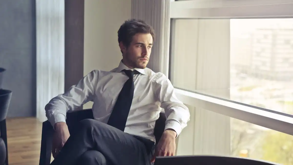 An executive sitting thoughtfully in a calm modern office, gazing out a floor-to-ceiling window.