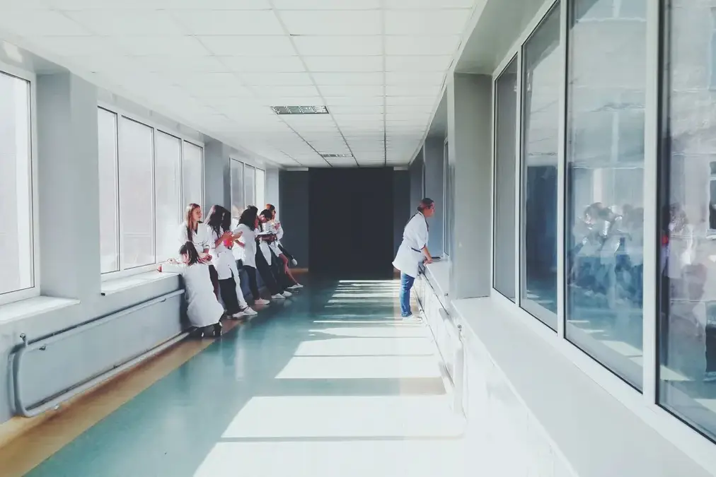 A physician standing alone in a quiet hospital corridor beside a window