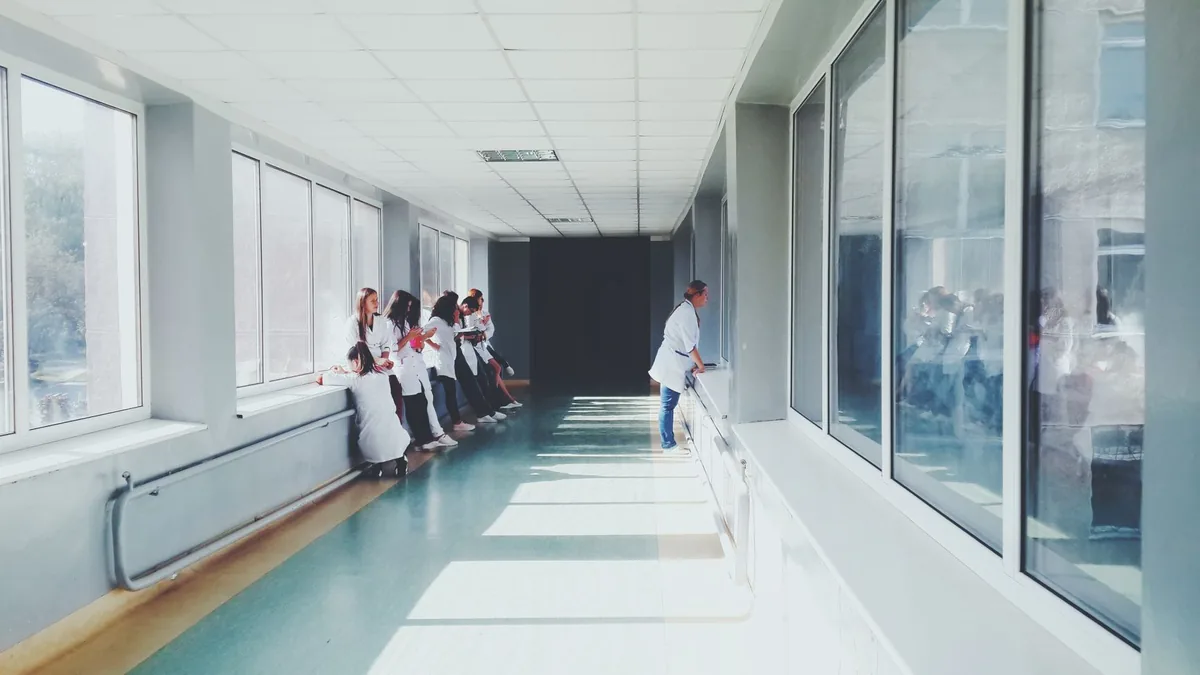 A physician standing alone in a quiet hospital corridor beside a window