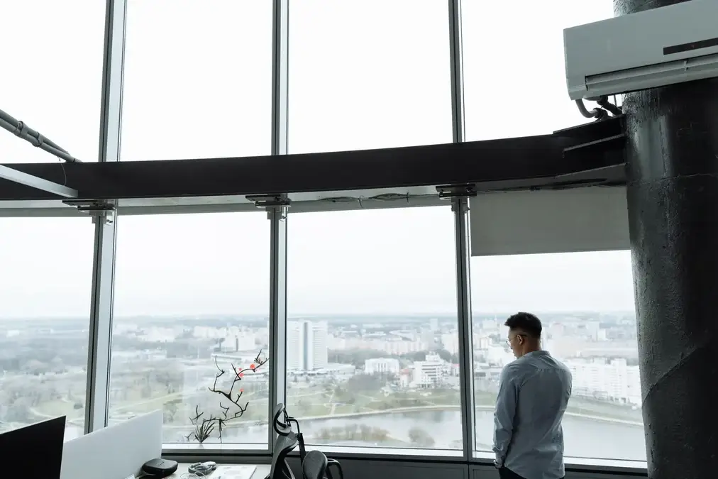A senior executive standing alone by an office window at dusk