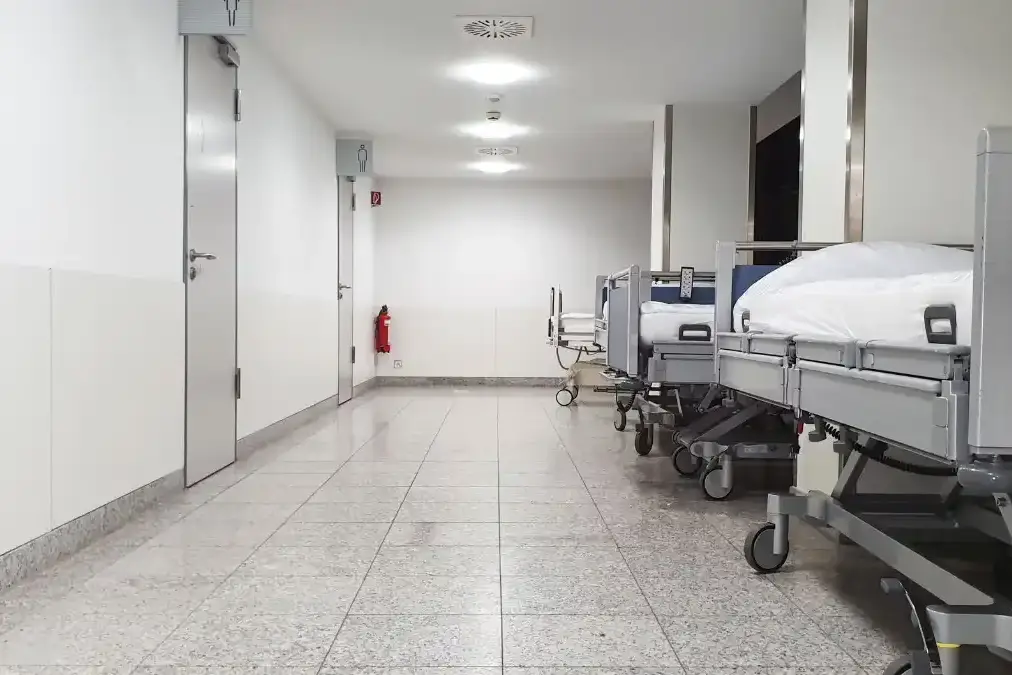 A physician in a white coat pausing alone in a quiet hospital corridor.