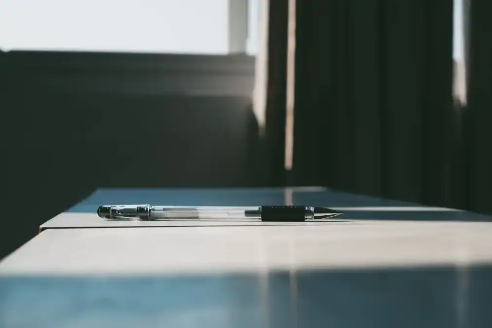 A writer sitting alone at a desk near a window with a notebook and warm light.