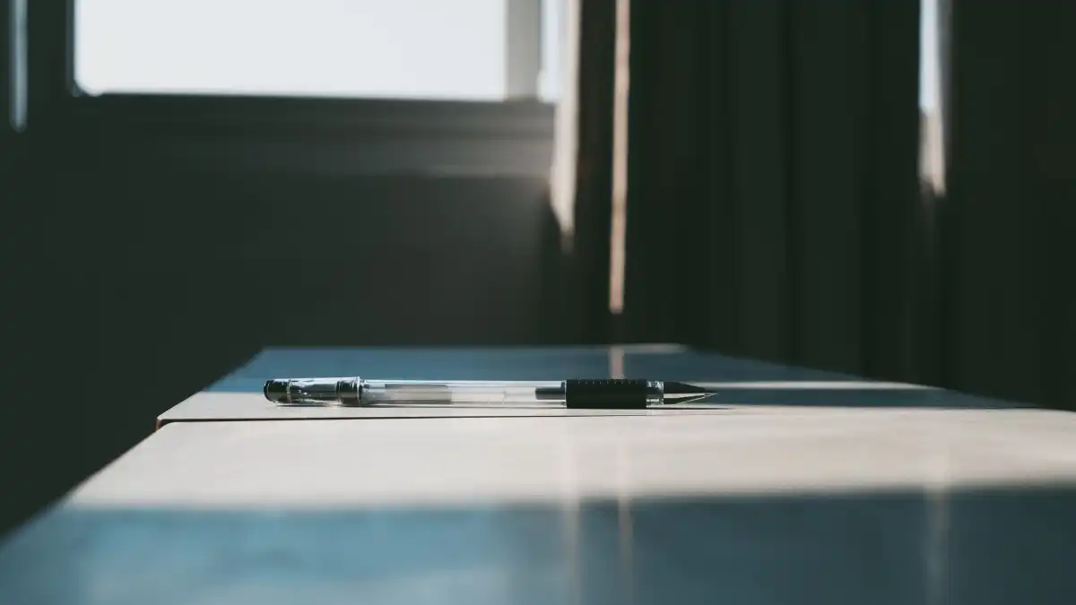 A writer sitting alone at a desk near a window with a notebook and warm light.