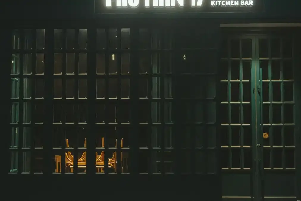 A chef stands alone in a dim, empty restaurant kitchen after service, leaning on a steel counter.
