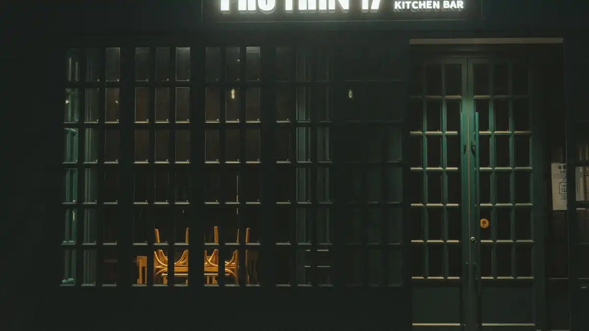 A chef stands alone in a dim, empty restaurant kitchen after service, leaning on a steel counter.