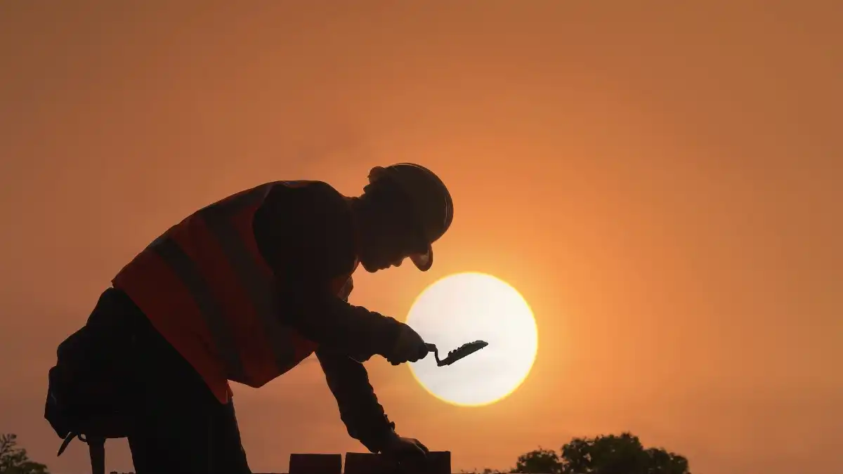 A construction executive in a hard hat looks out over a quiet building site at dawn, deep in thought.