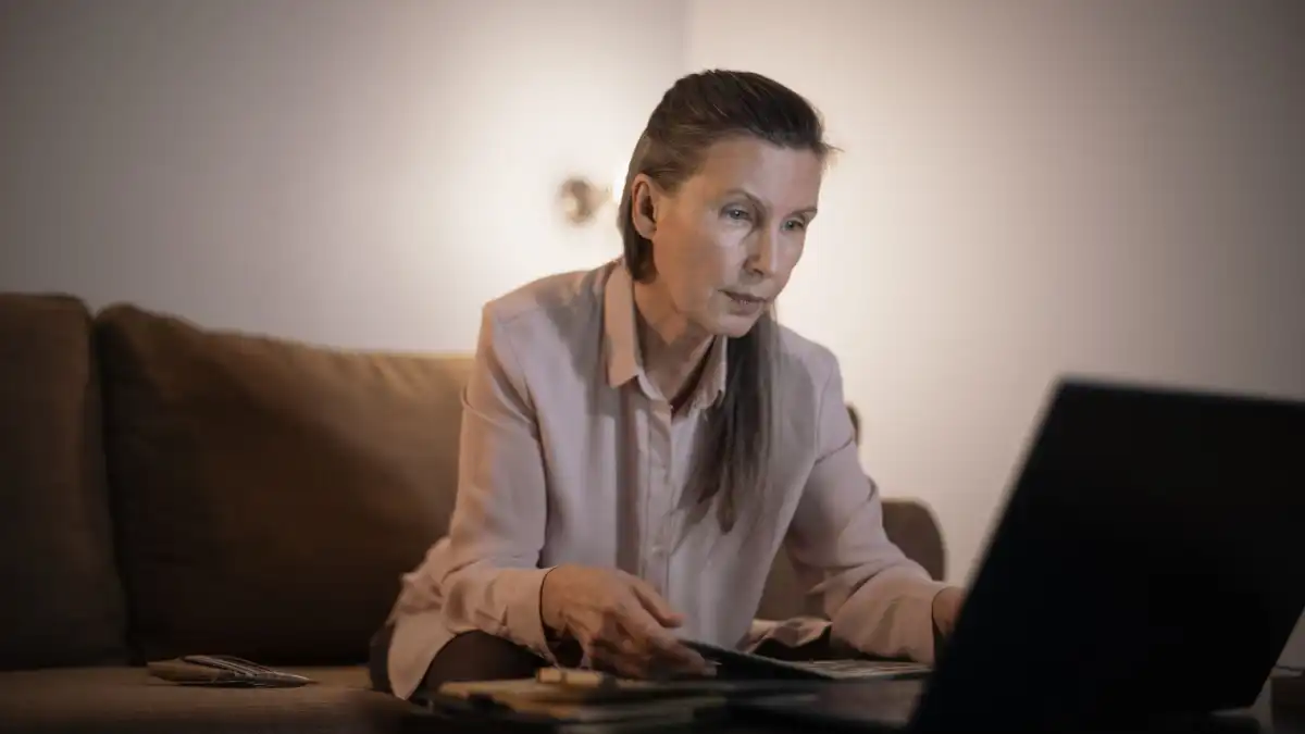 An executive sits alone in a dim study at night, wedding ring visible, looking down in quiet thought.